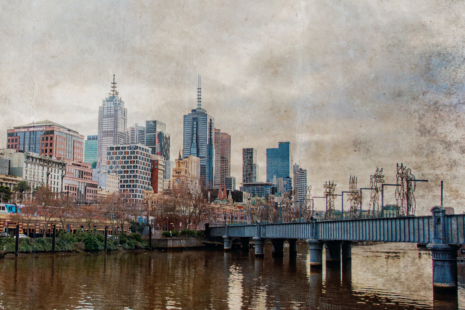 A river view with a sculptural bridge in the foreground and dense city buildings beyond.